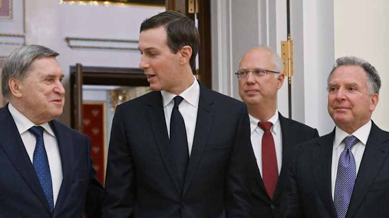 Ušakov, Kushner, Dmitrijev ja Witkoff seisovat tummissa puvuissa ja erivärisissä kravateissa suuren oven edessä.