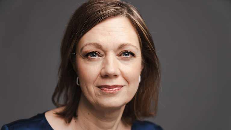 Kuvassa on nainen, joka katsoo kameraan. Hänellä on yllään sininen paita.