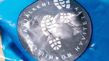 Sininen pakkaus, jossa on mustavalkoinen logo, jossa näkyy kengänjälki. Teksti logossa on "HIILIJALJALKENI ON HYVITETTY."