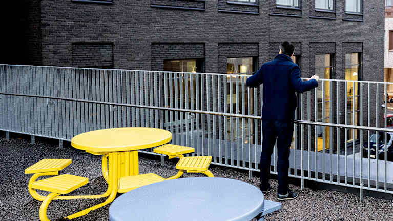 Juhana Brotherus selkä kameraan kohti ulkona etualalla värikkäitä pöytäryhmiä.