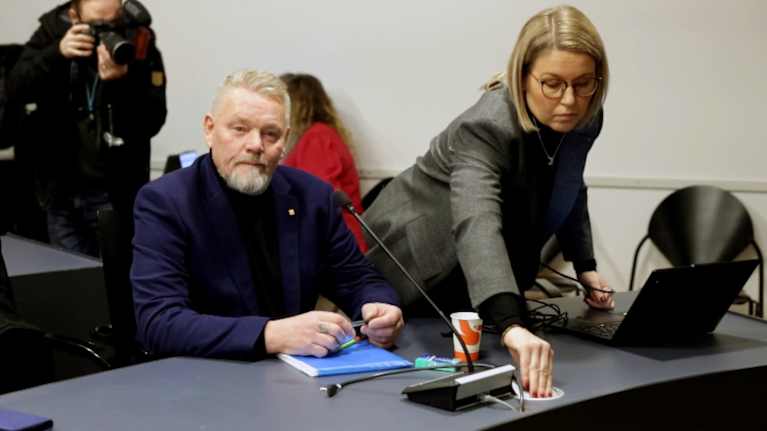 En man och en kvinna deltar i ett möte, där kvinnan hjälper mannen med något tekniskt på datorn.