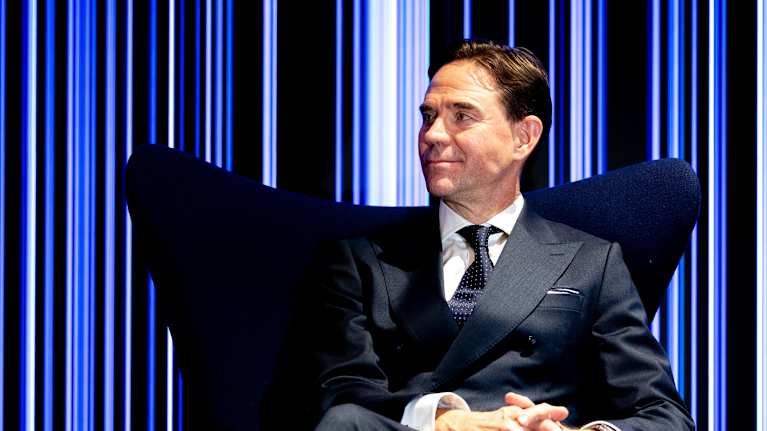 Jyrki Katainen istuu yön sinisessä nojatuolissa valoseinän edessä jossa eri sävyisiä sinisiä viivoja.