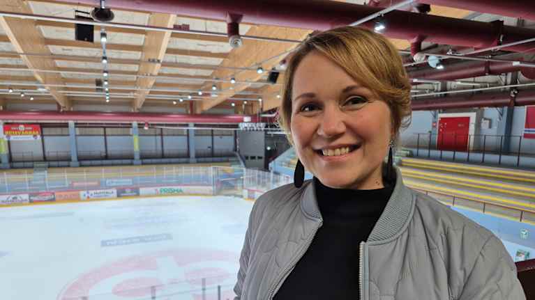 Hymyilevä nainen nojaa kaiteeseen jäähallin ylälehterillä.