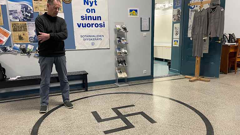 Kuvassa rehtori katsoo koulun lattiassa olevaa hakaristiä Iisalmen Lyseossa.