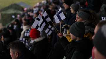 Ihmisiä katsomossa. Yhdellä pojalla kädessä kolme Suomen lippua.