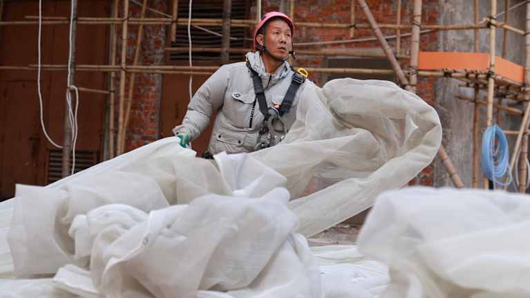 Rakennusmies poistaa viranomaisten määräyksestä paloarkaa suojaverkkoa työmaalta Hongkongissa.