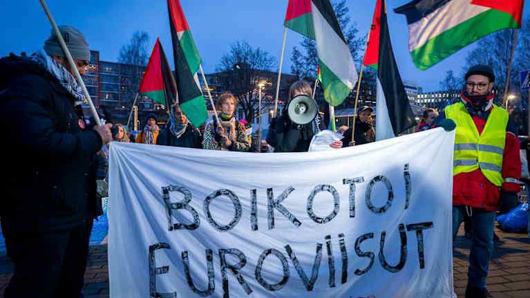 Mielenosoitus, jossa osallistujat kantavat palestiinalaisia lippuja ja banderollia, jossa lukee 'Boikotoi Euroviisut'."