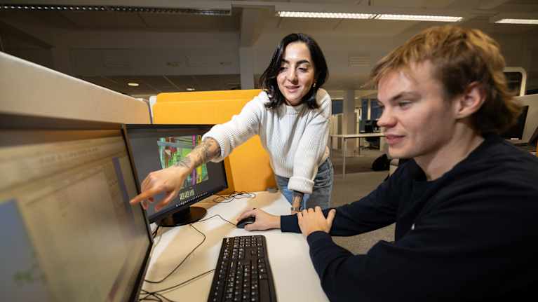 Jasmin on kollegansa vieressä pääteruutujen äärellä. Käsi osoittaa näytöltä jotain.