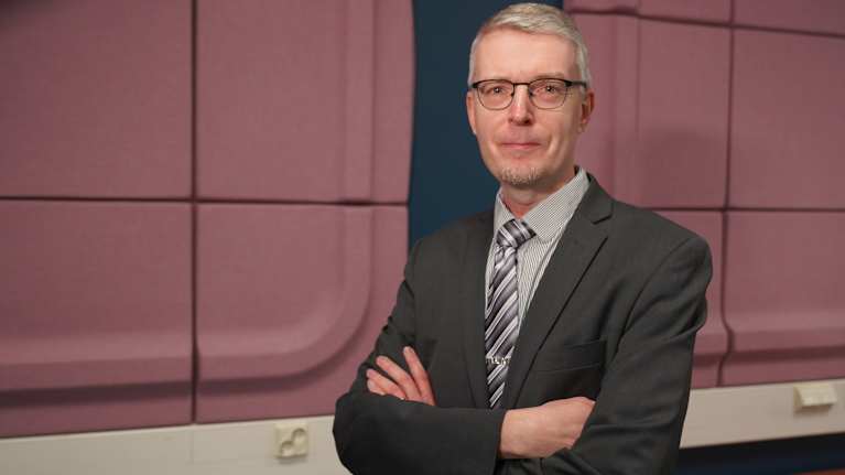 Tomi Voutilainen, Julkisoikeuden professori, Itä-Suomen yliopisto seisoo YLE:n aulatiloissa kameraan katsoen punertavan seinän edessä .