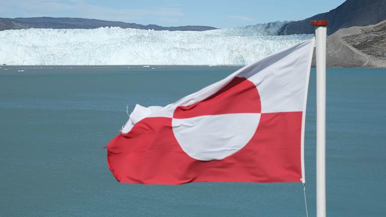 Grönlannin lippu liehuu, taustalla jäätikköä ja merta.