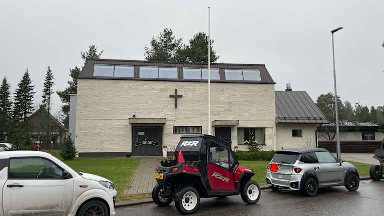 Talo, jonka seinässä risti, edustalla autoja.