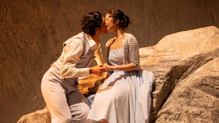 Nainen ja mies istuvat kivellä ja suutelevat toisiaan.