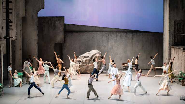 Tanssiryhmä on näyttämöllä ja takaosan lavasteena on suuri kivenlohkare. 