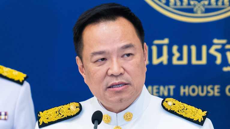 Mies valkoisessa univormussa puhuu mikrofoniin ja katsoo kohti lehdistöä.