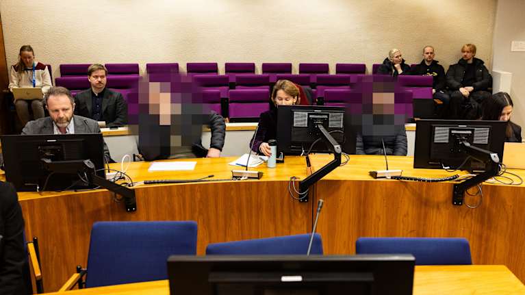 Henkilöitä istumassa oikeussalissa. Kahden henkilön osalta kuvaa on käsitelty ja heidän kasvonsa on sumennettu.