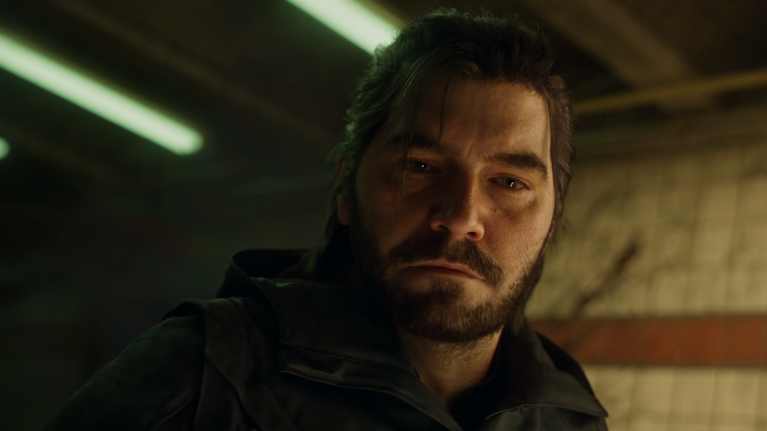 Videopelissä mies katsoo kameran suuntaan vakavan näköisenä.