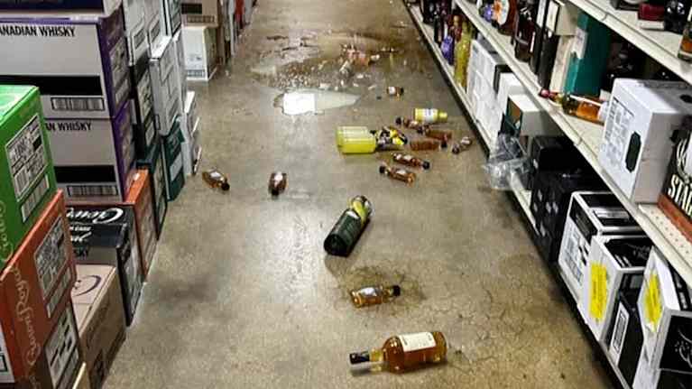 Rikkoontuneita pulloja alkoholikaupan lattialla pesukarhun jäljiltä.