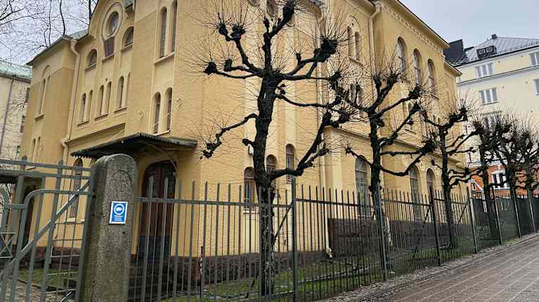 Keltainen kivirakennus rauta-aidan takana. Rakennus toimii synagogana. 