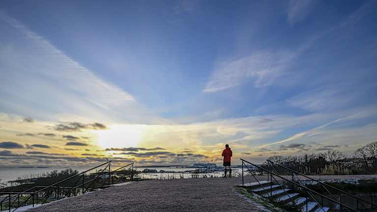 Mies seisoo hupparissa Kaivopuistossa merta katsellen.