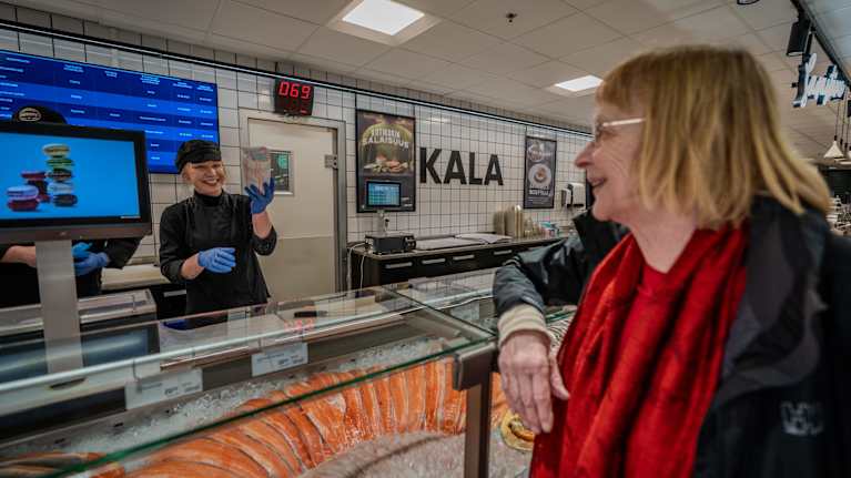 Nainen ojentaa kalapaketin asiaakkaalle.