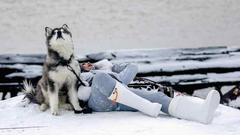 Nainen makaa lumisella laiturilla koiran vierassä Teriberkassa.