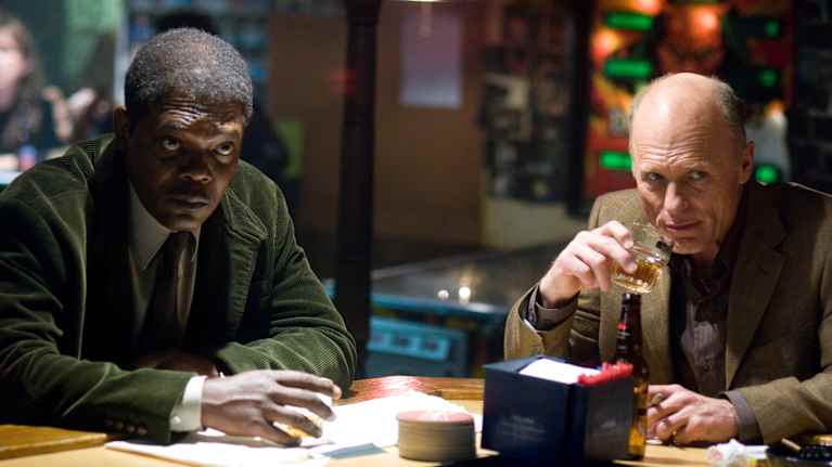 Musta ja valkoinen mies istuvat baaritiskillä ja katsovat johonkin kuvan ulkopuolella.