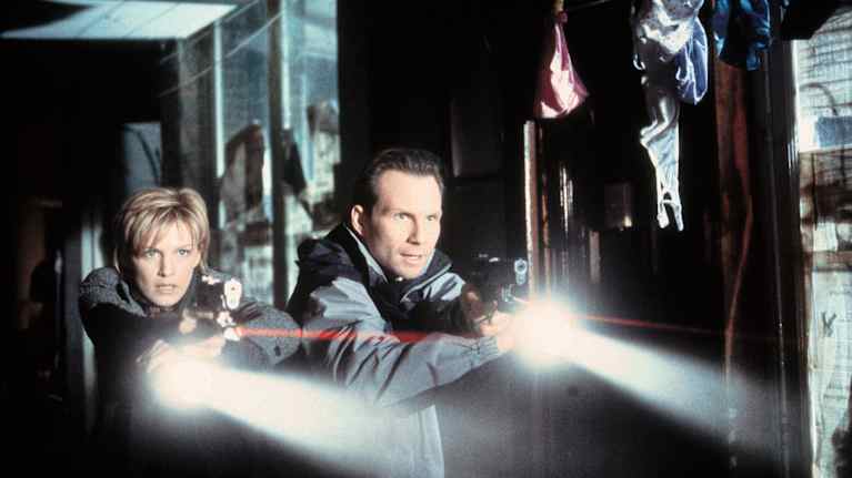 Valkoinen nainen ja valkoinen mies osoittavat aseilla ja taskulampuilla johonkin pimeässä.