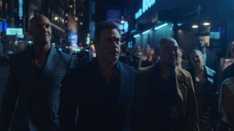 Kolme miestä kävelee rinnakkain öisen kadun ihmisvilinässä