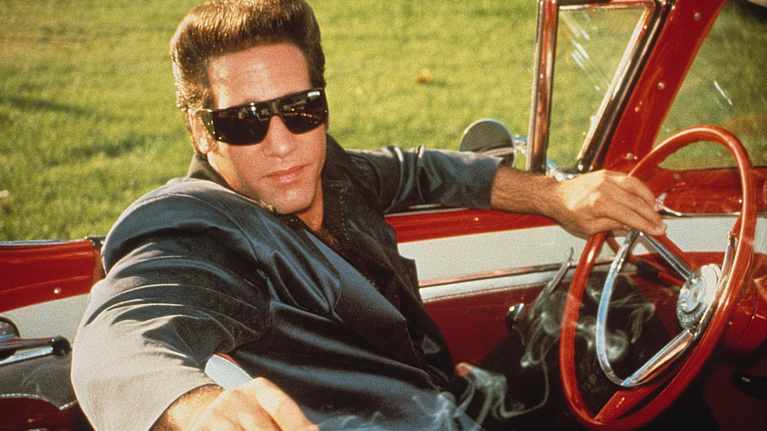 Andrew Dice Clay roolissa elokuvassa Ford Fairlane. Hän istuu avoauton etupenkillä aurinkolasit silmillään.