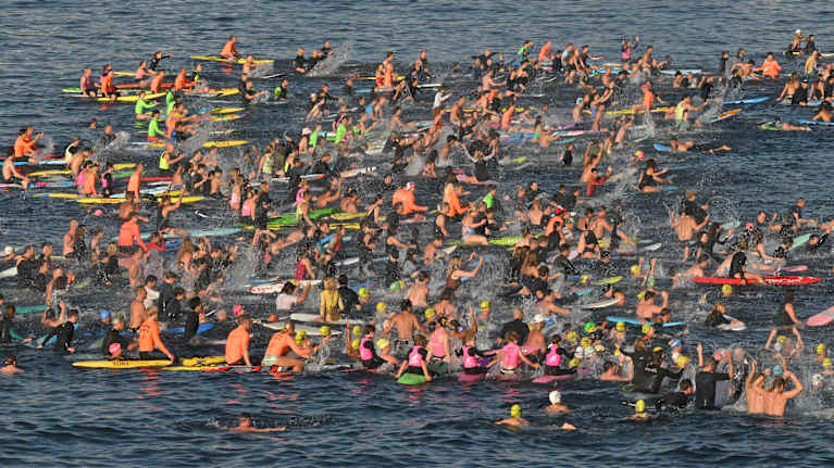 Satoja ihmisiä kelluu meressä surffilaudoilla.