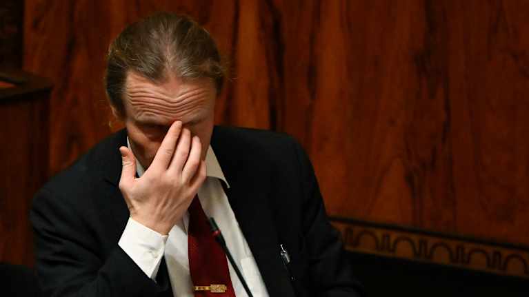 Juho Eerola istuu eduskunnassa käsi kasvojensa edessä.