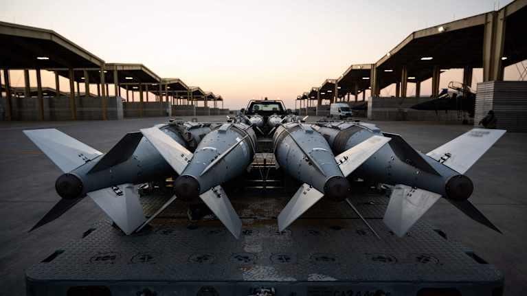 Neljä ohjusta, jotka ovat rivissä kuljetusalustalla. Taustalla näkyy katettu rakennelma ja hämärtyvä taivas.