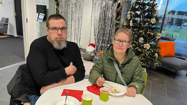 Kaksi ihmistä ruokailee, taustalla on joulukuusi.
