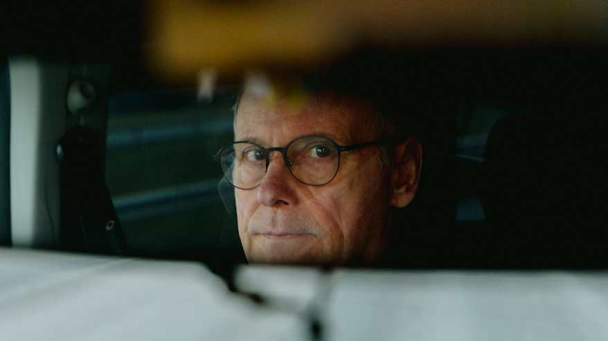 Henkilö heijastuu auton taustapeilistä.