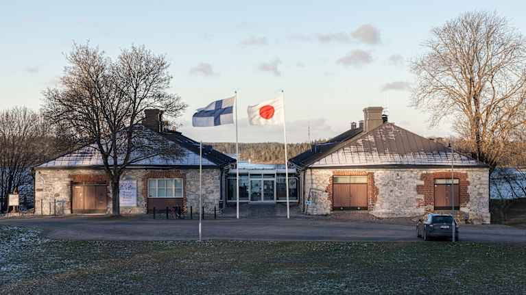 Kuvassa on rakennus, jonka edustalla liehuu kaksi lippua: Suomen ja Japanin lippu.