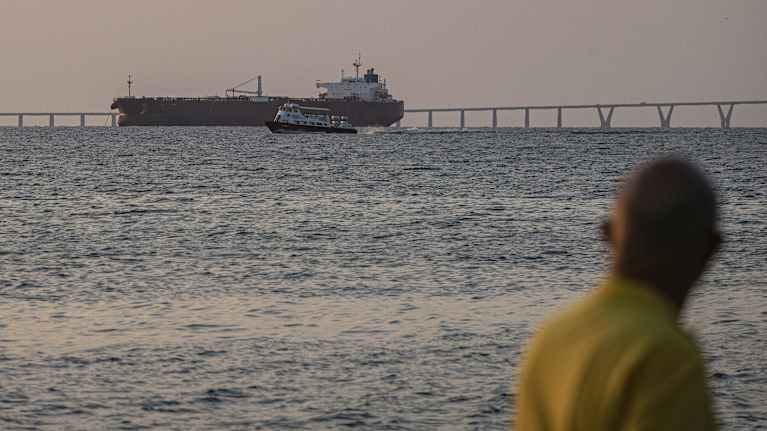 Mies katselee merellä olevaa tankkeria, vieressä suurta laituria.