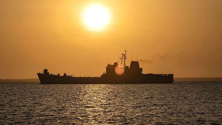 Sotalaiva näkyy iltavalaistuksessa merellä, laskeva aurinko.