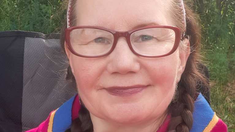 Valentina Sovkina on pukeutunut värikkääseen asuun. Kaulassaan hänellä on riipus, jossa on saamelaiskuvio.