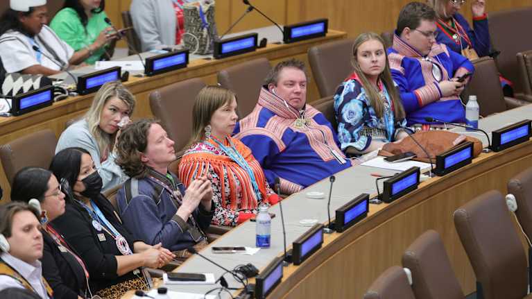 Salissa pöytien takana istuu eri alkuperäiskansojen edustajia, muun muassa joukko saamelaispukuisia henkilöitä.