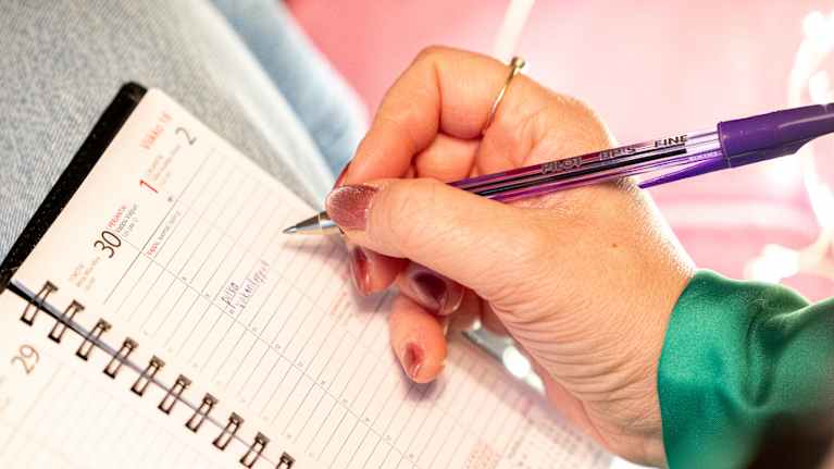 Henkilön kädessä kynä, paperisessa kalenterissa vapun kohdalla lukee pitkä viikonloppu.
