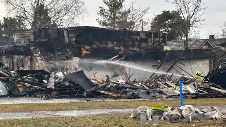 Palaneen rakennuksen rauniot, joita pelastustyöntekijä suihkuttaa vedellä.