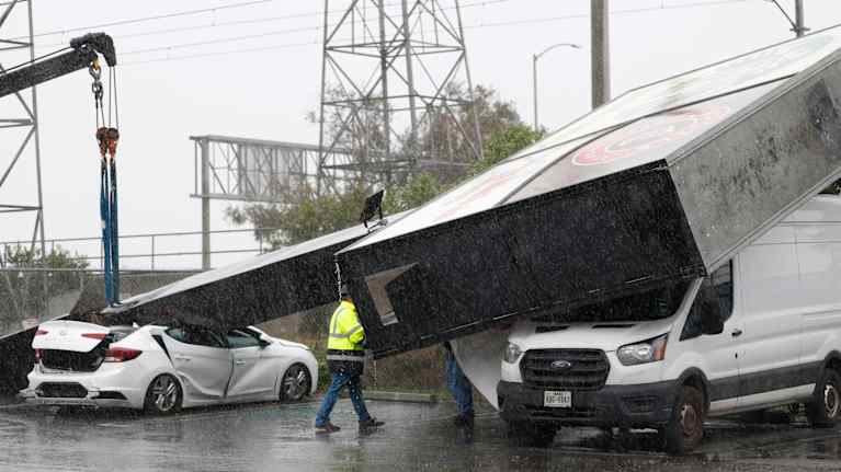 Suuri mainoskyltti on kaatunut kahden auton päälle. Vettä sataa.