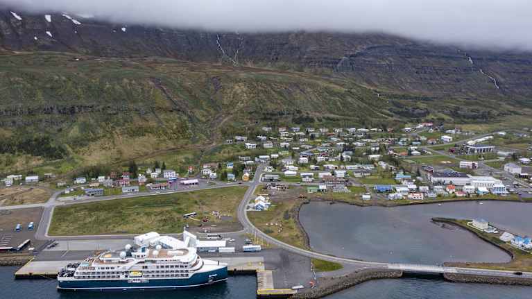 Ilmakuva Seyðisfjörðurista: edustalla merta ja laiva, taustalla rakennuksia. Takana nousee vuori.
