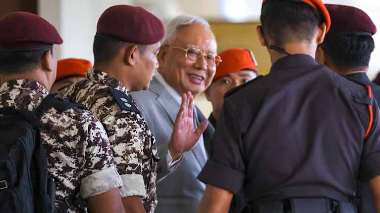 Malesian entinen pääministeri Najib Razak vilkuttaa kameralle sotilaiden ympäröimänä.