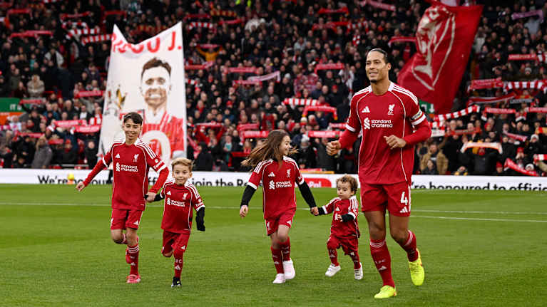 Jalkapalloilija Virgil van Dijk saattaa maskottilapset ulos kentältä ennen Liverpoolin pelin alkua.