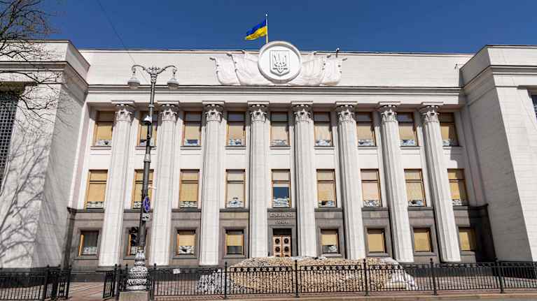 Ukrainan parlamenttirakennus aurinkoisena päivänä. Katolla liehuu Ukrainan lippu.