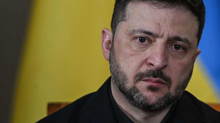 Volodymyr Zelenskyi lähikuvassa, taustalla Ukraina lippu. Vakava ilme.
