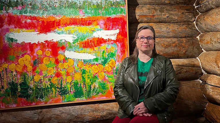 Nainen istuu värikkään maalauksen edessä.