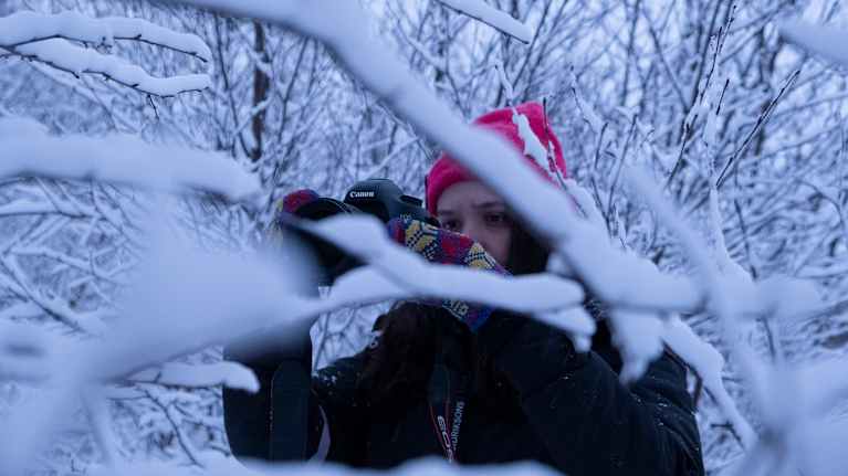 Lada Suomenrinne valokuvaamassa ulkona lumisten oksien takana. 