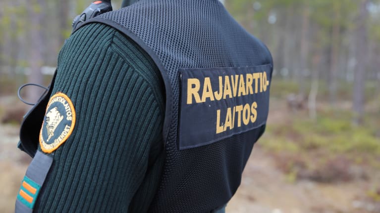 Rajavartija seisoo selin ja paidan selässä lukee rajavartiolaitos.